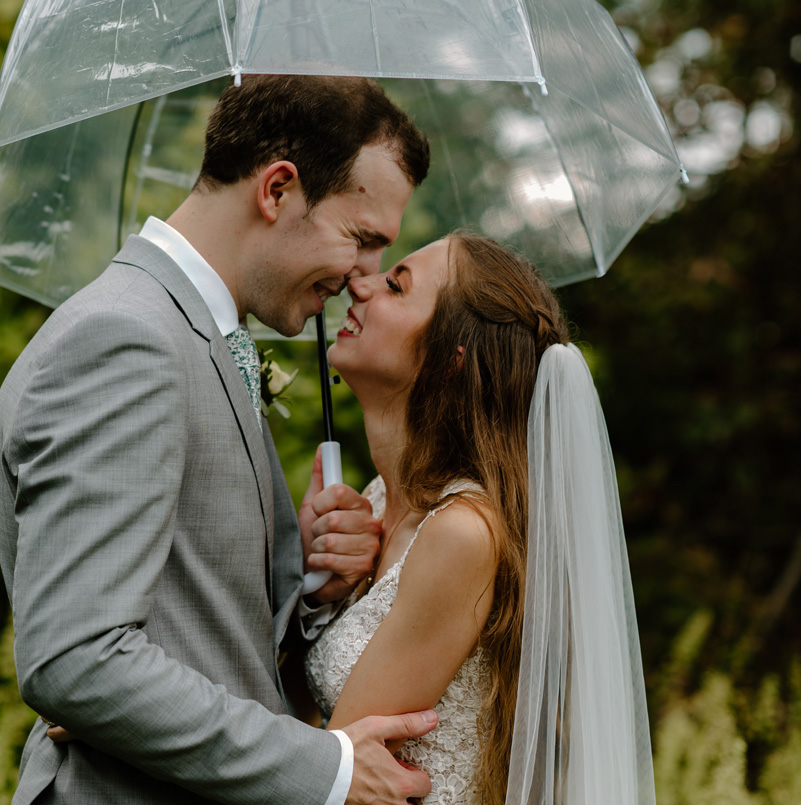Bride and groom cuddle underneath an umbrella on their rainy summer wedding day in Illinois