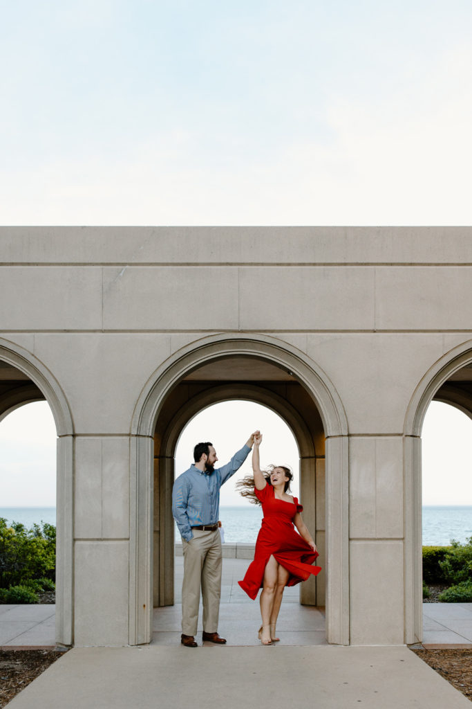 a man twirls a woman under an arch with lake michigan in the background