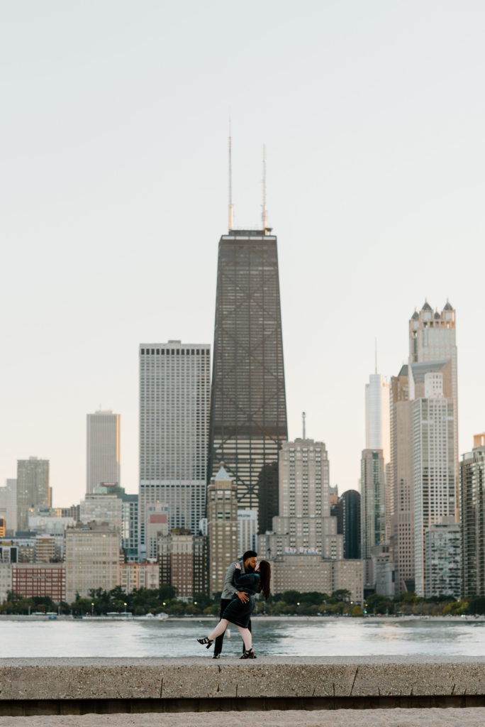 man dips his fiancé at north avenue beach with the chicago skyline in the background