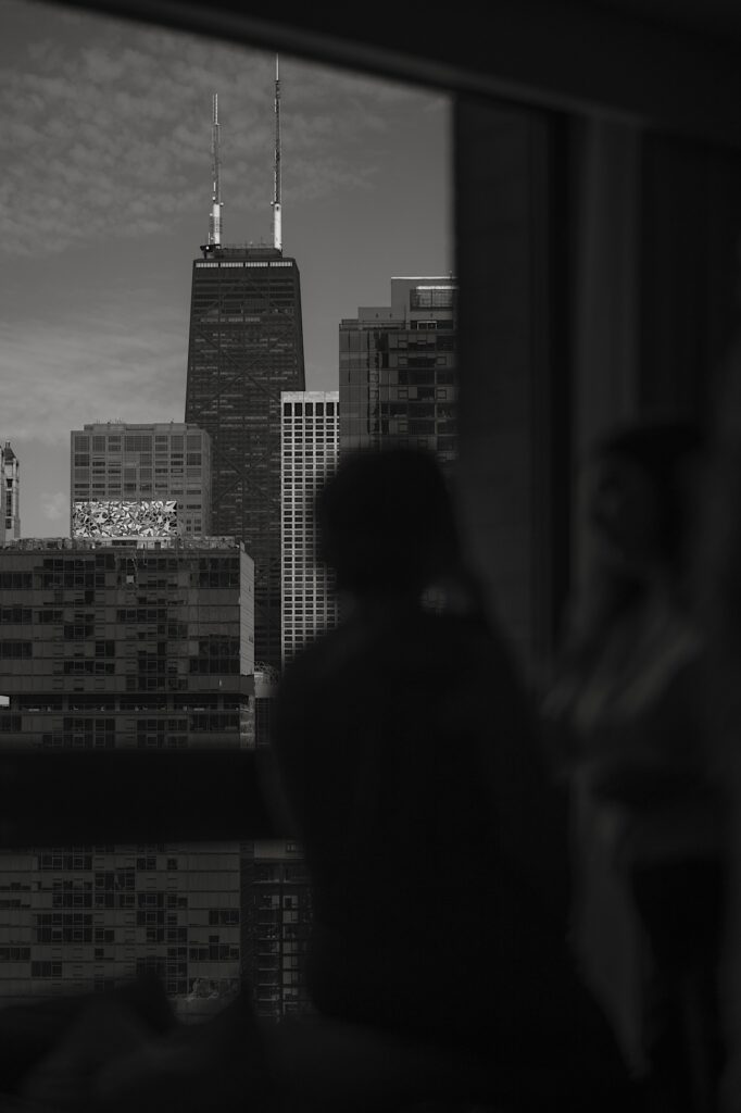 A bride looks out the window towards the sky scrapers of Chicago including the John Hancock building.