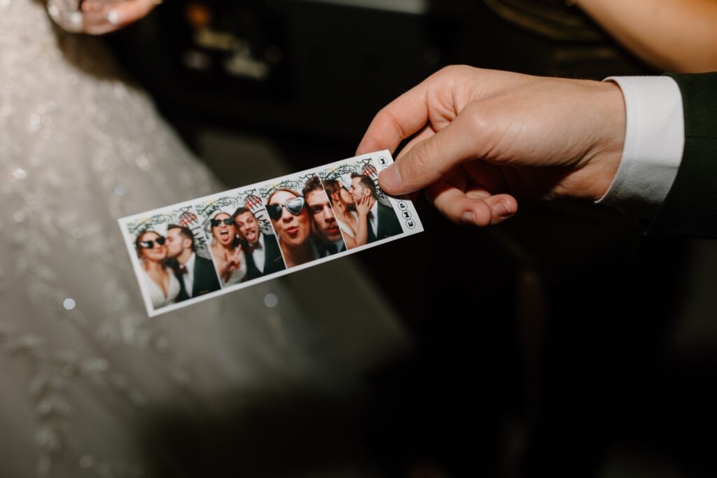 A bride and groom use the photo booth at Emporium on their wedding day in Chicago.  The bride wore heart shaped glasses for the photos and behind them there is graffiti covering the photobooth.