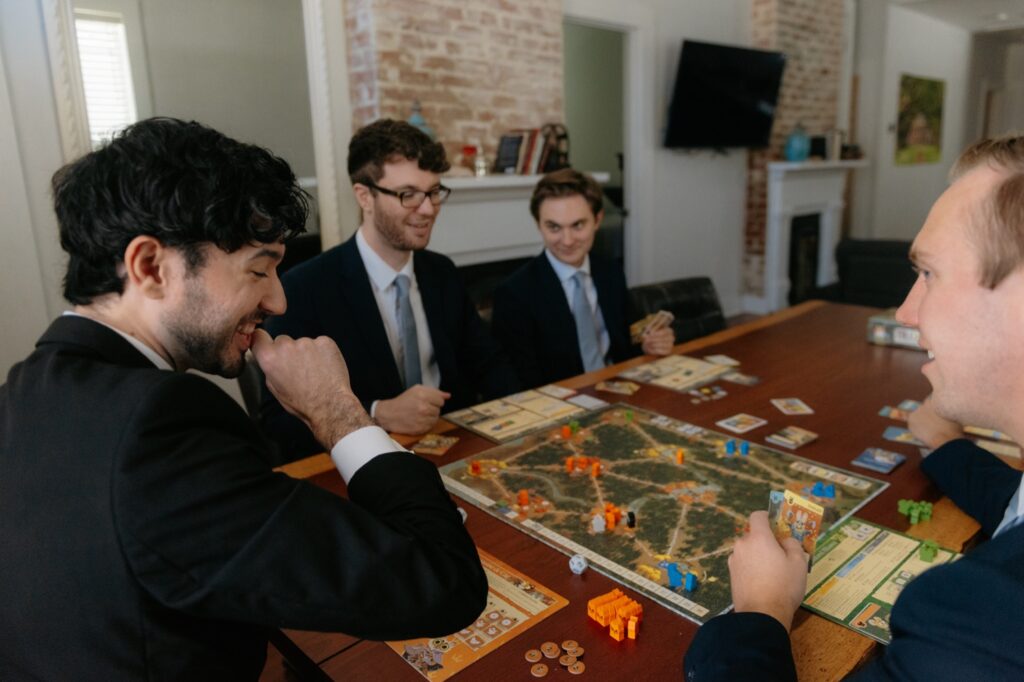 A groom plays a game with his groomsmen play a round of Root at their Chicago Airbnb before heading out for the wedding ceremony.