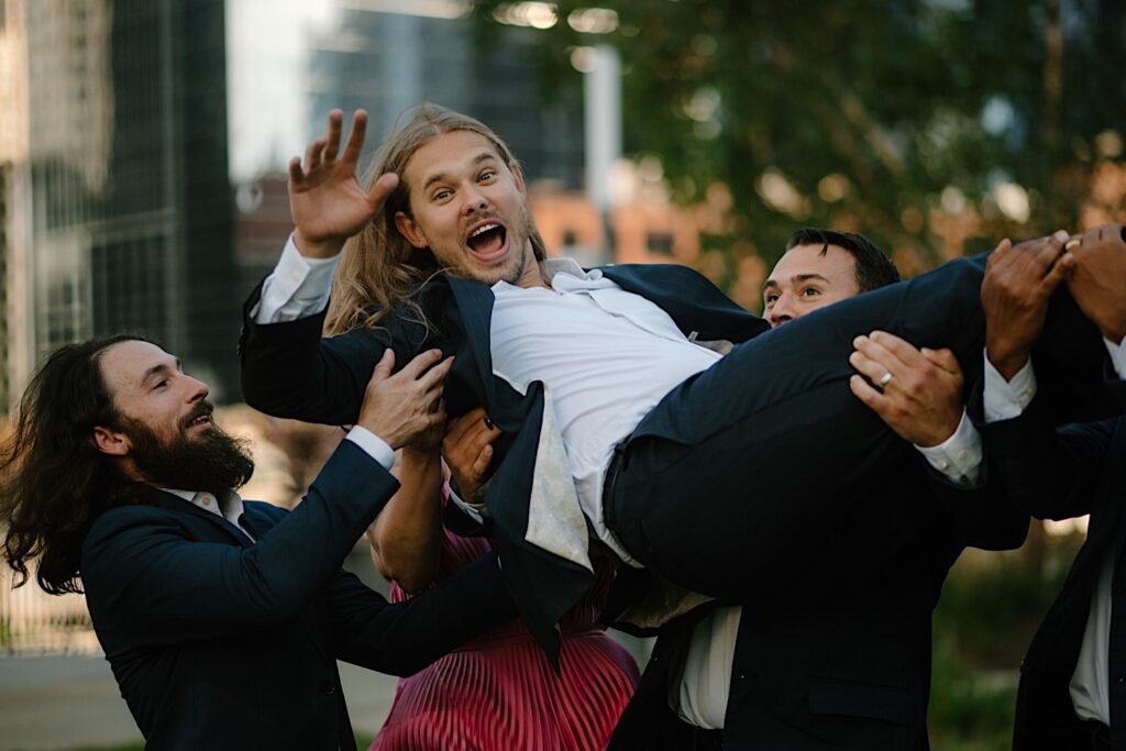 A groom is carried by his wedding party in Chicago for wedding party portraits surrounded by skyscrapers.