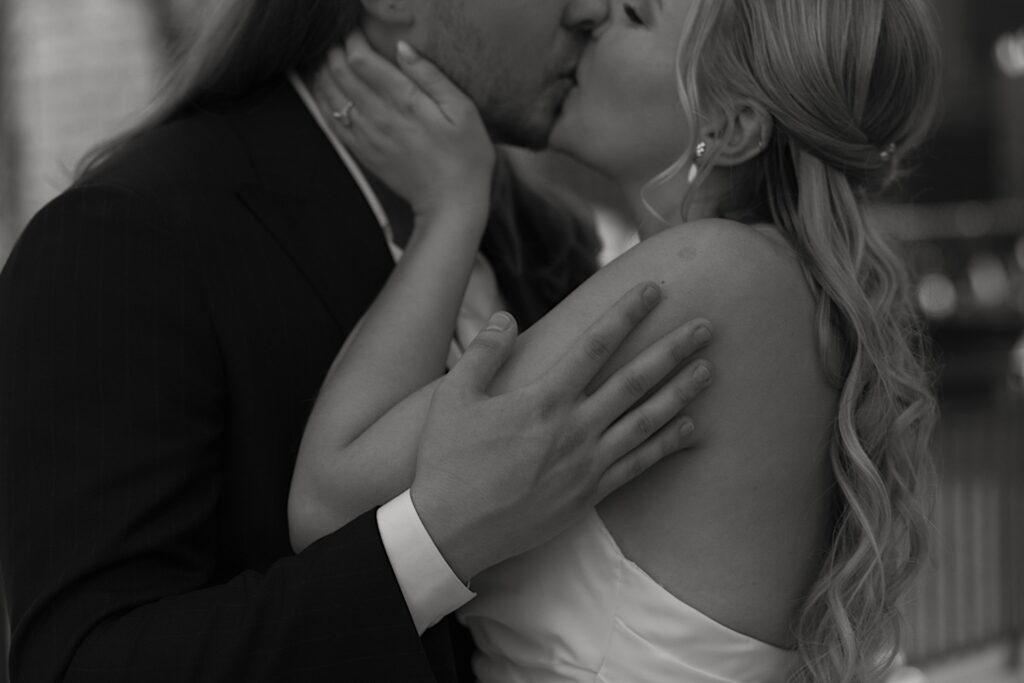 A bride and groom hold each other and passionately kiss overlooking the Chicago river.  The image is in black and white and is just of the upper body of the newly-weds.