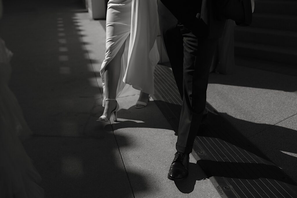 The legs of a bride and groom walking together through the streets of Chicago in a black and white image.