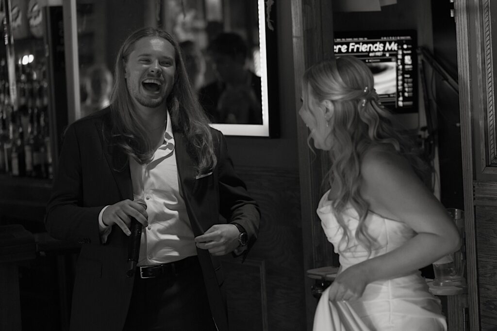 A groom laughs with his bride as they sing a song in a dive bar in Chicago on their wedding day with their wedding party.