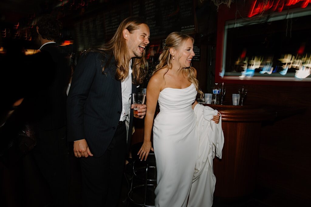 A bride and groom laugh together while watching their guests celebrate them at their favorite karaoke bar in Chicago.