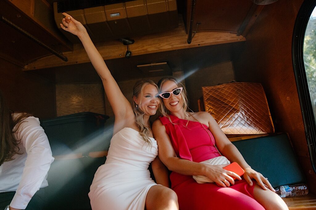 A bride poses with a bridesmaid celebrating her wedding day on a Chicago Trolley.  The bridesmaid is wearing a hot pink bridesmaid dress and a pair of light pink glasses.