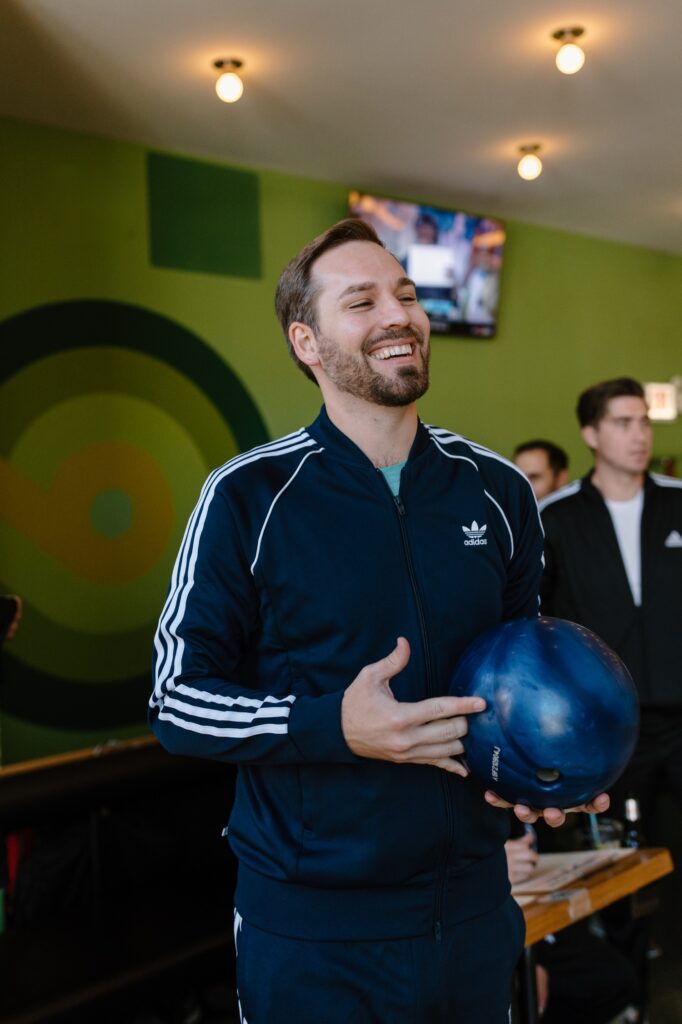 A groom fits in a round of bowling the morning before his wedding with his groomsmen at Avondale Bowl in Chicago.  They're all wearing matching Adidas jump suits and bowling shoes.