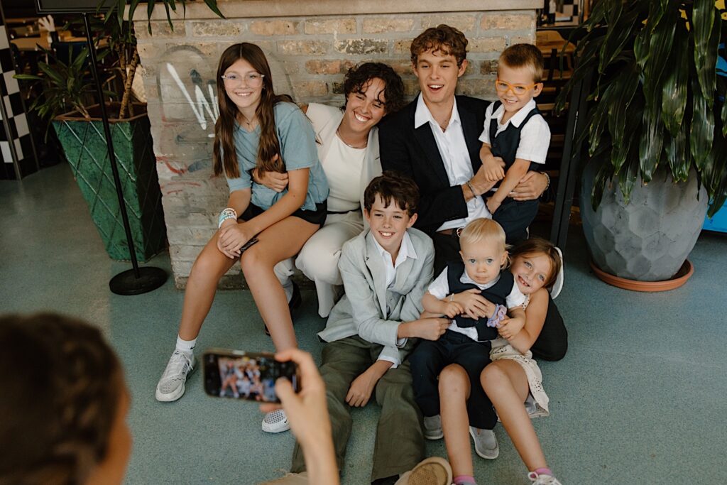 Wedding guests pose for a group picture sitting on the ground together at a rooftop wedding venue in Chicago.