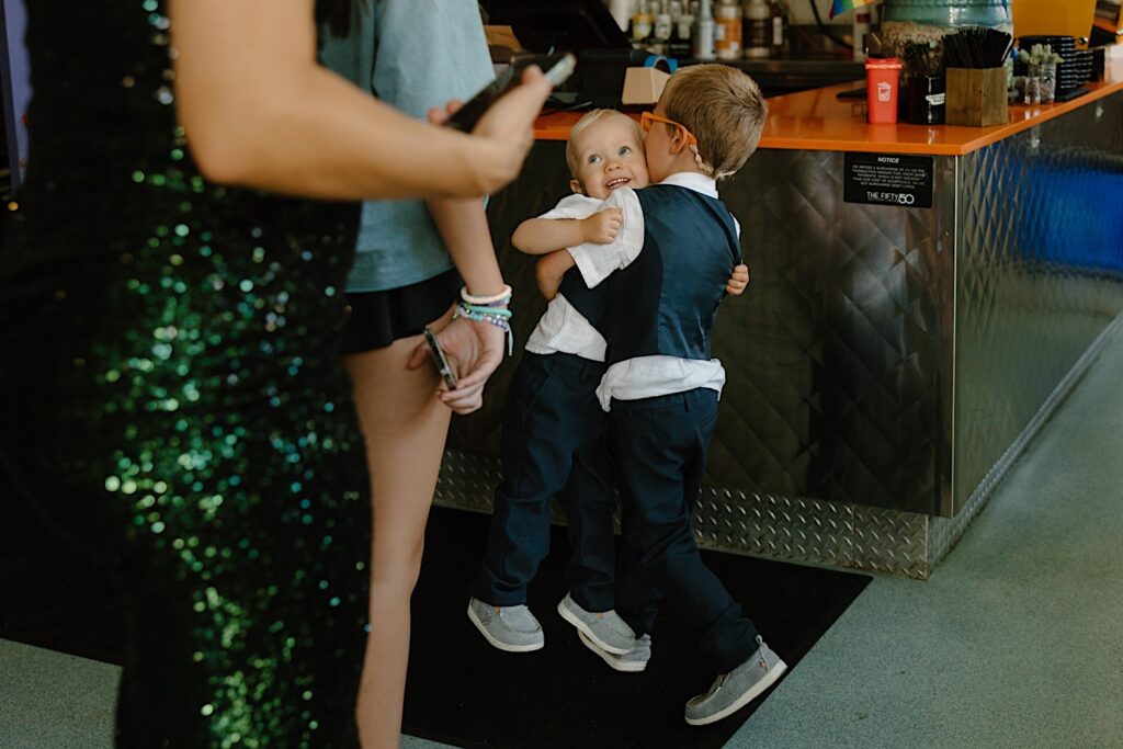 Two ring bearers wrestle with one another wearing boat shoes, and shortsleeved white button ups with vests.  They're attending a wedding at Homestead on the Roof.