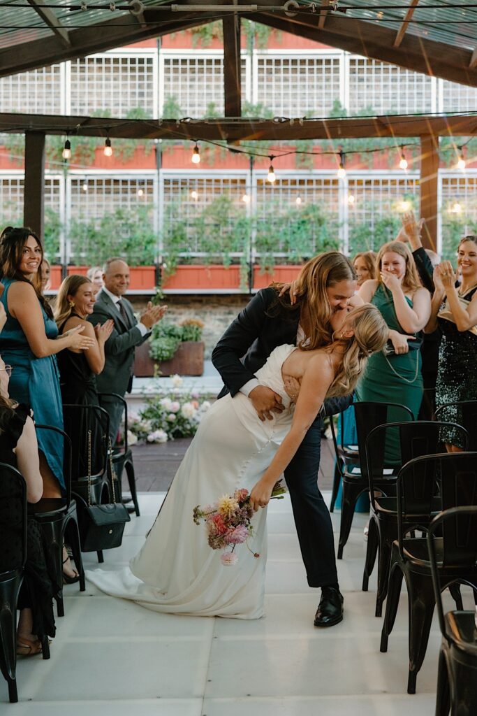 A groom dips his bride as they walk down the aisle after their Chicago rooftop wedding ceremony at Homestead on the Roof. 