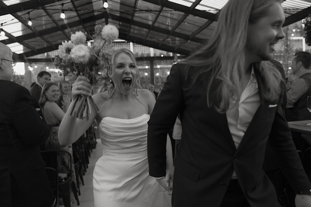 A bride celebrates and looks at the camera as she leaves her the ceremony space of her wedding venue Homestead on the Roof. 