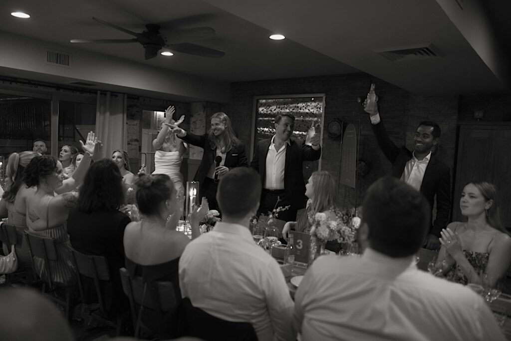 The bride and groom enter their wedding reception inside Homestead on the Roof surrounded by guests.  The groom gives a toast to their guests. 