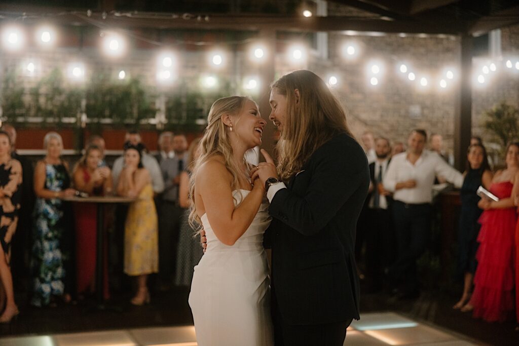 A bride and groom share a first dance on a lit dance floor that is lined with their guests for their first dance.  The rooftop wedding venue in Chicago is lit with string lights and the lighting within the dance floor. 