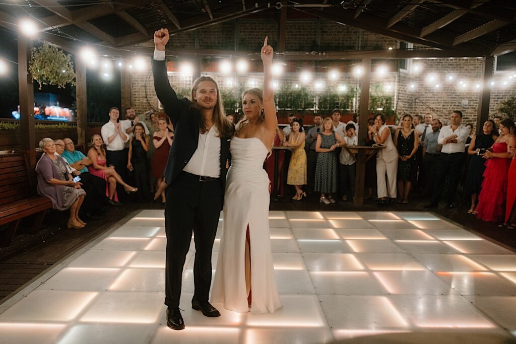 A bride and groom share a first dance on a lit dance floor that is lined with their guests for their first dance.  The rooftop wedding venue in Chicago is lit with string lights and the lighting within the dance floor. 