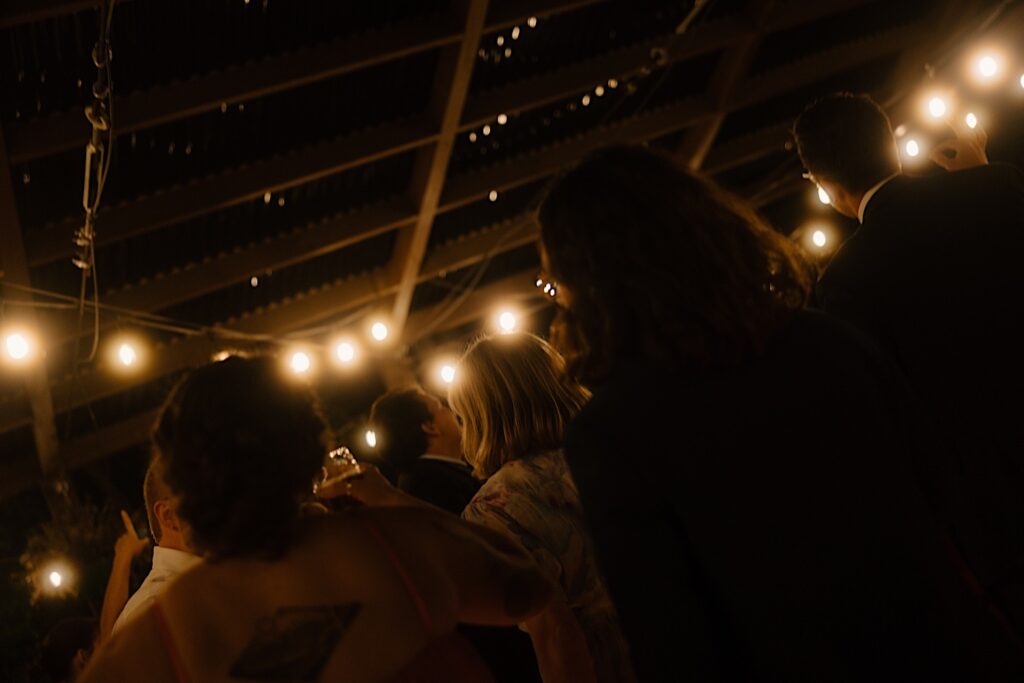 A crooked image of guests rushing the dance floor of a Chicago rooftop wedding venue lined with string lights. 