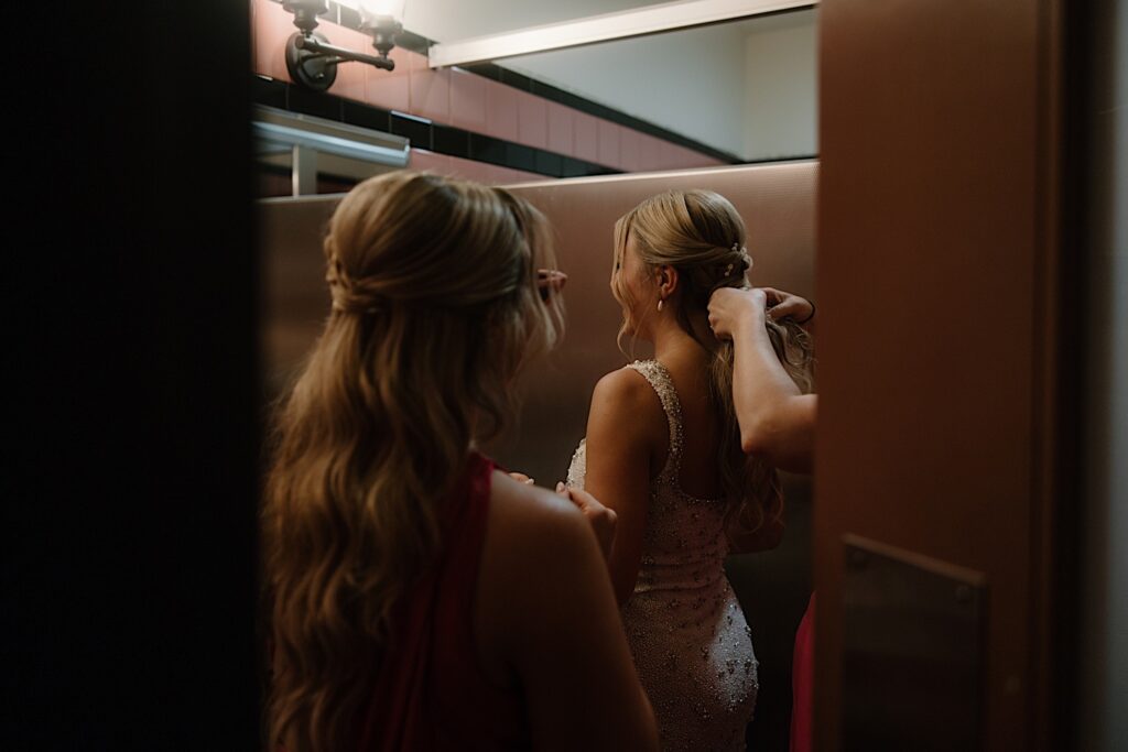 A bride has her bridesmaid put her hair up in a pony tail before returning to the dance floor on her wedding day.  She changed into her reception outfit which is a beaded gown designed by Clio Peppiatt.