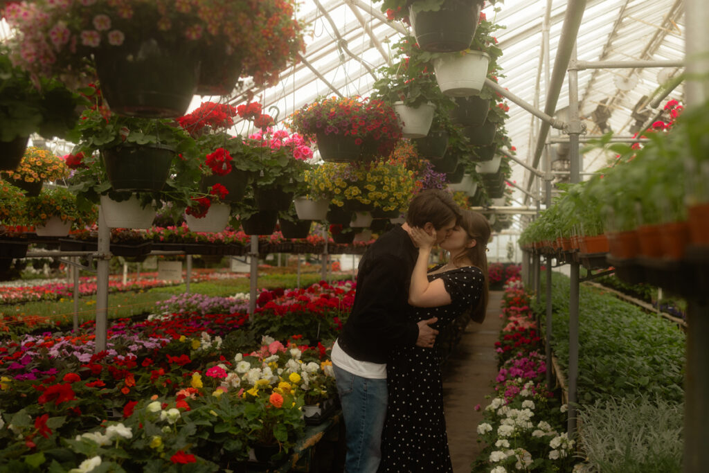couple kissing in a garden center surrounded by flowers.