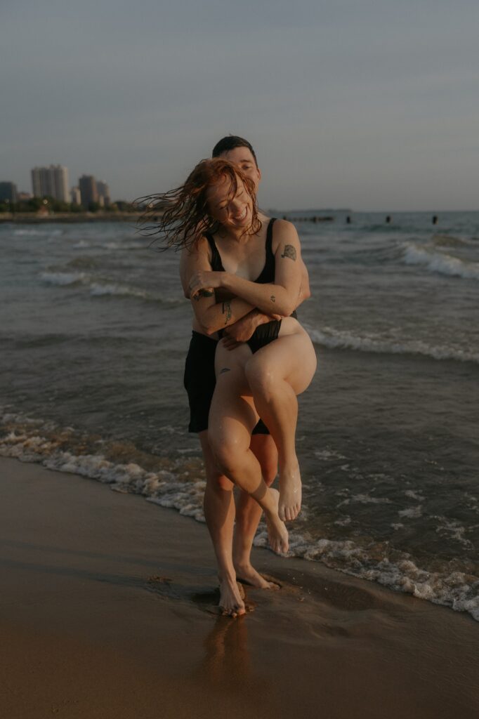 A woman smiles as a man carries her from behind while the two are in swim suits on North Avenue Beach in Chicago